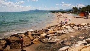 Une plage au rivage rocheux, où l’on peut voir des gens se prélasser au soleil, et un ciel dégagé.