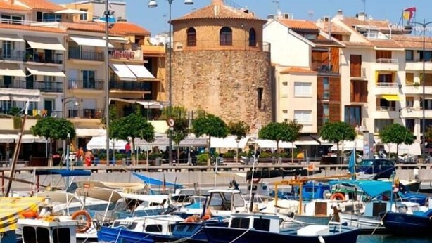 Un port de plaisance avec des bateaux amarrés, une tour en pierre et des immeubles résidentiels dotés de balcons.