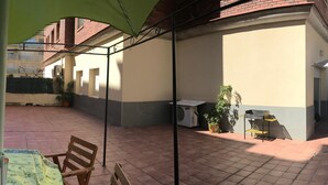 Un patio couvert avec un banc en bois, une table recouverte d’une nappe et un barbecue.