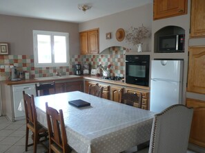 A kitchen with a dining table, chairs, a refrigerator, an oven, a microwave, and a coffee maker.