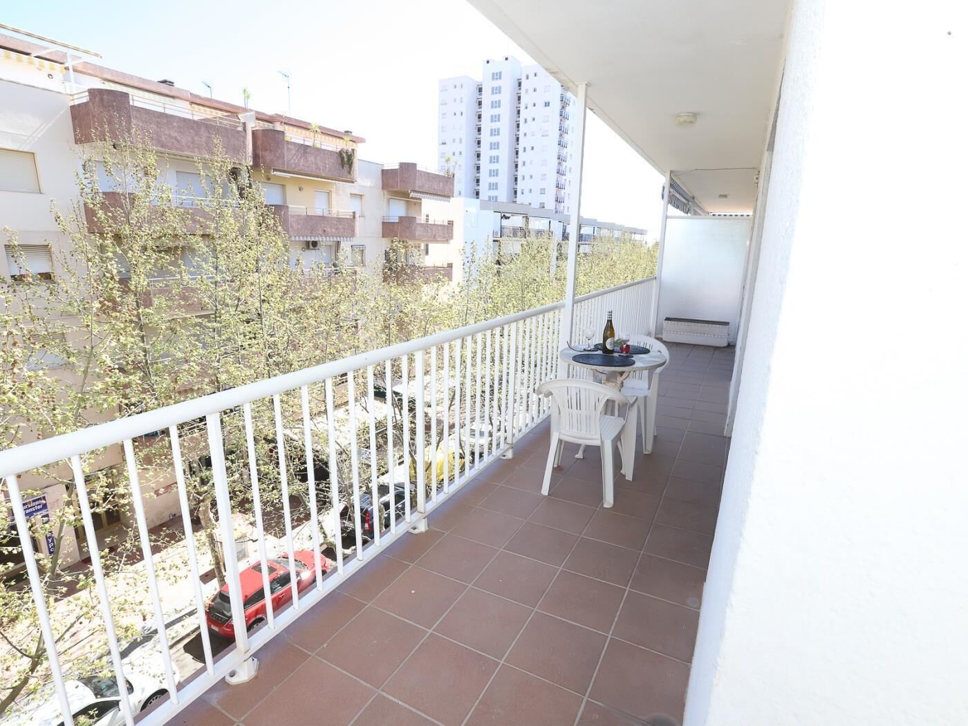 A balcony with a white railing, a small table with chairs, and a bottle of wine.