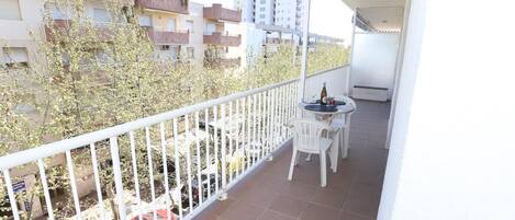 A balcony with a white railing, a small table with chairs, and a bottle of wine.