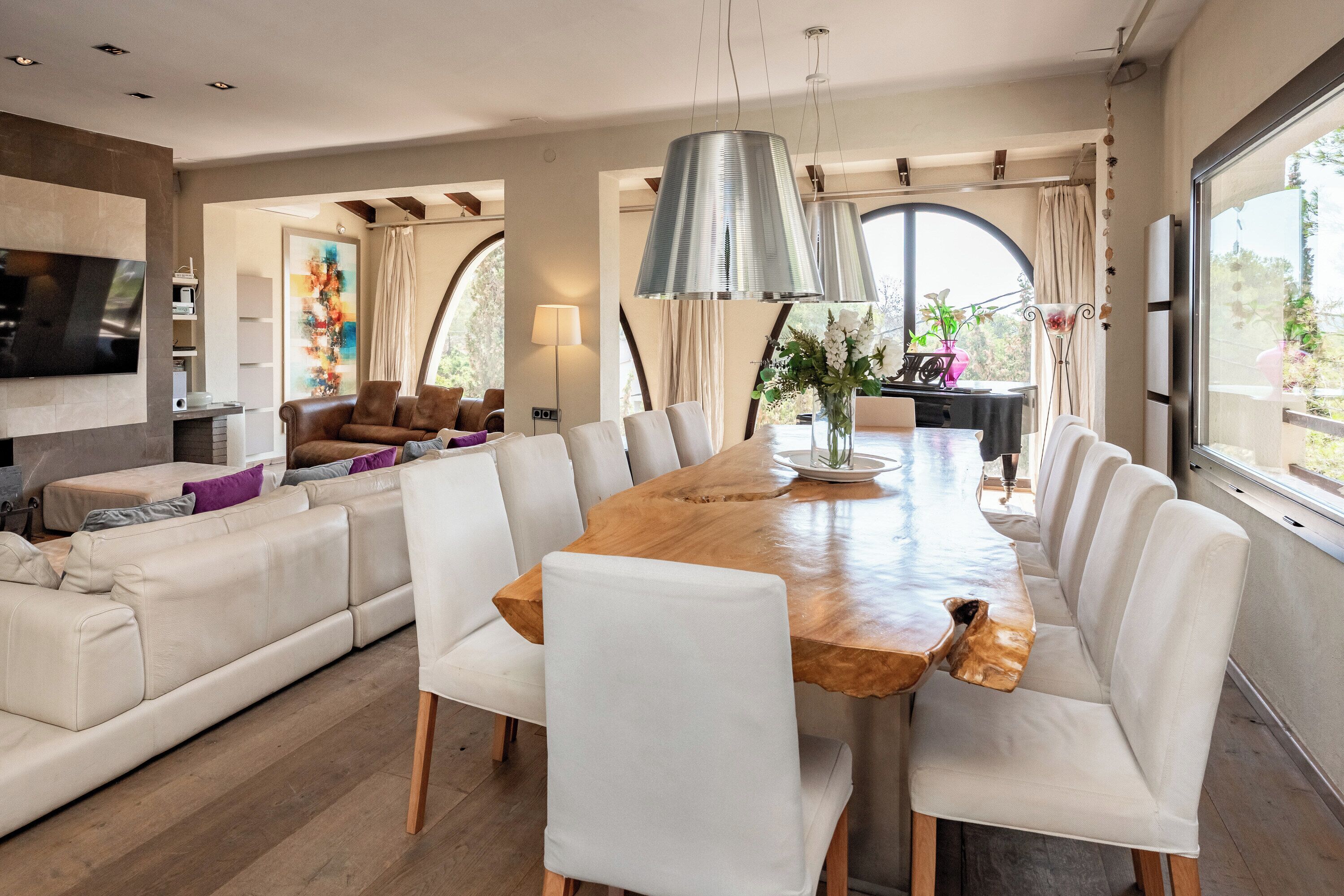 Un salon moderne avec une grande table à manger en bois, des canapés blancs et un téléviseur fixé au mur.
