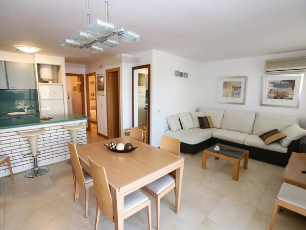 Een moderne woonkamer met een houten eettafel, een bank en een keuken met aanrecht en kasten.