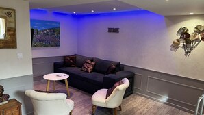 A modern living room with a dark sofa, two armchairs, a small round table, and a wall-mounted artwork.