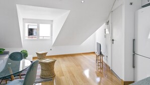 Eine moderne Küche mit weißen Schränken, einem Essbereich mit einem Glastisch und einem Fernseher auf einem Schrank.