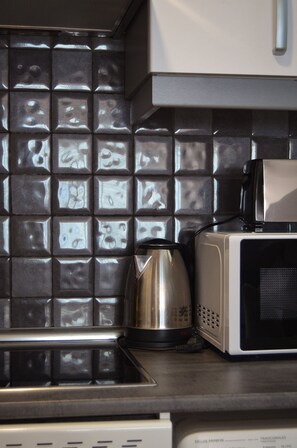 Une cuisine avec un mur recouvert de carreaux, une bouilloire et un four à micro-ondes.