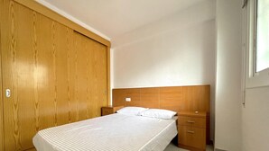 A single bed with a wooden headboard, a nightstand, a wooden wardrobe, and a window with daylight.