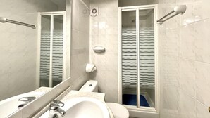 A bathroom with a sink, mirror, toilet, and shower.