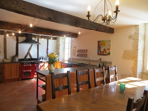 Uma cozinha rústica com vigas de madeira, um fogão vermelho e uma área de refeições com cadeiras e mesa de madeira.
