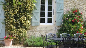 A stone building with a window, a table with chairs, and a potted plant. - Beautiful Stone Farmhouse With Heated Pool And Views Across Rolling Countryside (Gondrin)