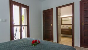 A bedroom with a bed, a window, and a bathroom visible through an open door. - Villa Comes - Beautiful villa with private pool 50 metres from the beach (Port d'Alcúdia)