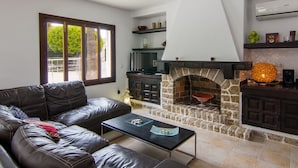 A modern living room with a stone fireplace, leather sofa, and a coffee table. - Villa Comes - Beautiful villa with private pool 50 metres from the beach (Port d'Alcúdia)