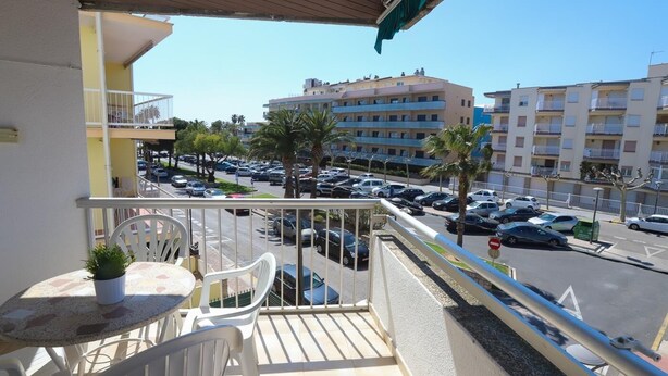 Un balcon avec une table et des chaises, donnant sur un parking et des immeubles.