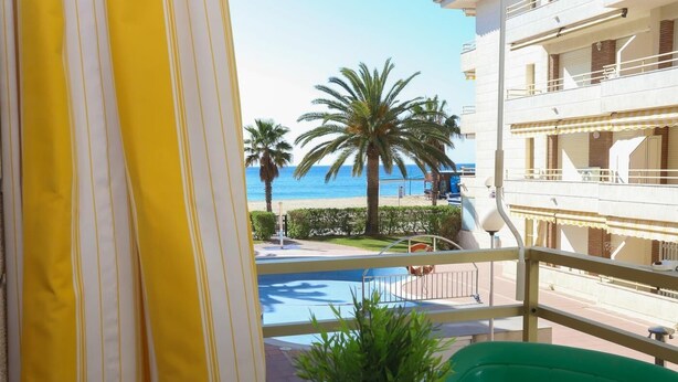A balcony with a view of a pool and palm trees, overlooking a beach.