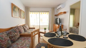 A cozy room with a sofa, a round dining table with placemats, a TV, and a small plant.