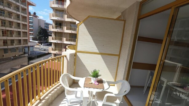 Un balcón con dos sillas blancas, una mesita y una planta en maceta.