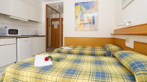 Habitación de hotel con cama, microondas, refrigerador pequeño, ducha y un cuadro en la pared.