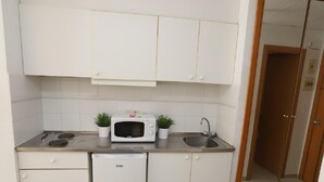 Una cocina compacta con armarios blancos, un microondas, un lavamanos y un refrigerador pequeño.