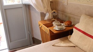 Un dormitori amb un llit, una taula de nit amb una làmpada, una tassa de cafè i un croissant.