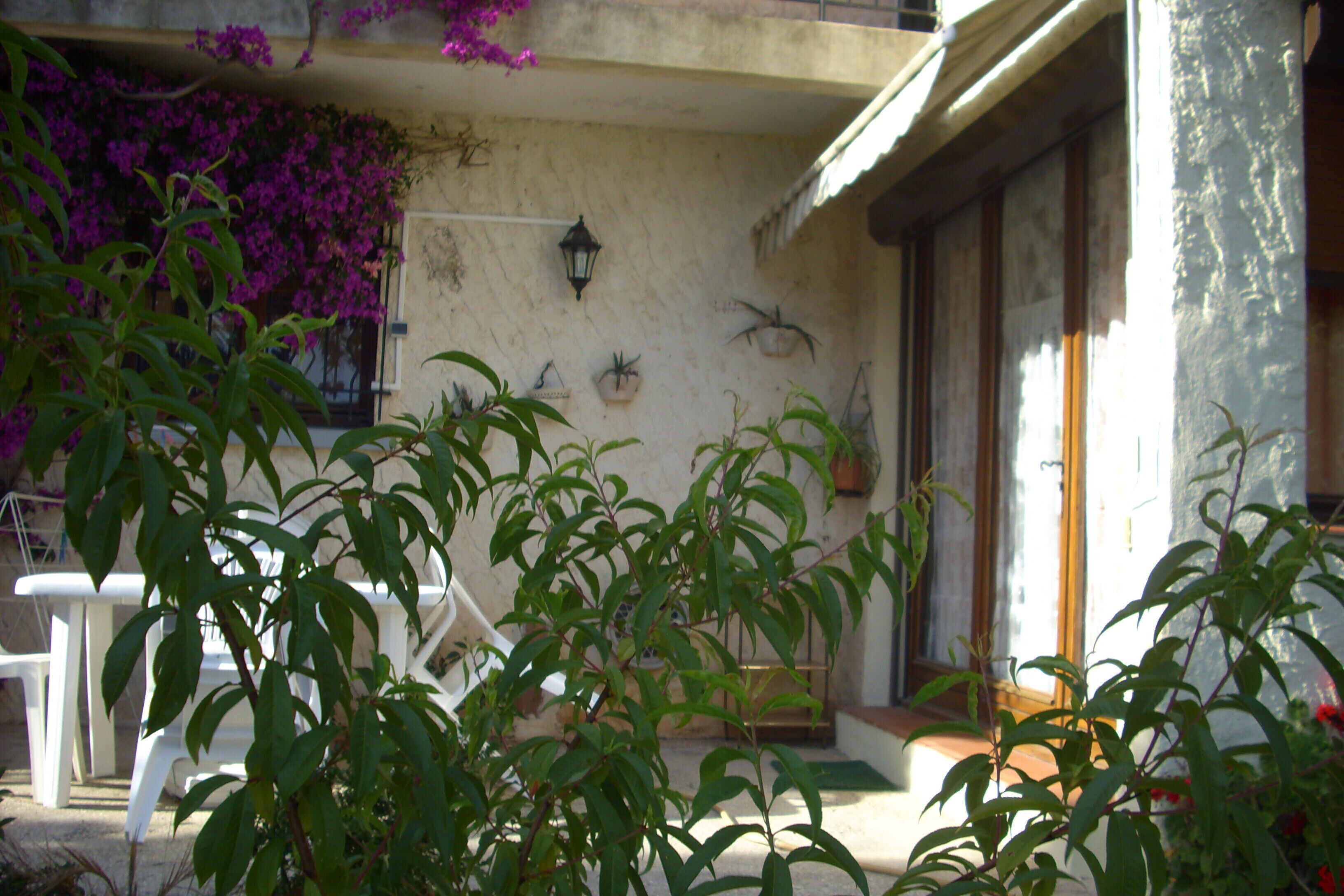 A building with a balcony, potted plants, and a white chair.