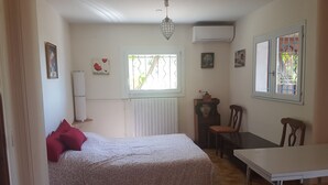 A bedroom with a bed, a table, a chair, a radiator, an air conditioner, and a window with bars. - GROUND FLOOR OF VILLA facing the tip of Giens (Carqueiranne)