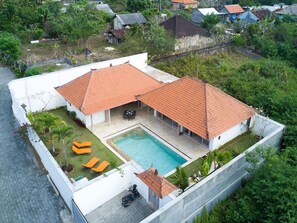 Una casa de dos pisos con piscina, un patio cubierto y un pequeño jardín.