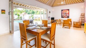 A dining area with a wooden table and chairs, a ceiling fan, and a view of the outdoor pool area. - Istana Willy (Ungasan)