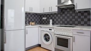 Una cocina moderna con armarios blancos, lavadora integrada, horno y campana extractora de acero inoxidable.