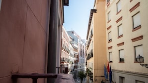 Una calle urbana estrecha flanqueada por edificios, un banco en primer plano y banderas en el edificio de la derecha.