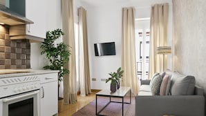 Una sala de estar moderna con un sofá gris, un televisor de pantalla plana y una cocina con estufa y armarios.