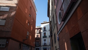 Un estrecho callejón urbano entre edificios con balcones, cielo despejado y una puerta visible al final.