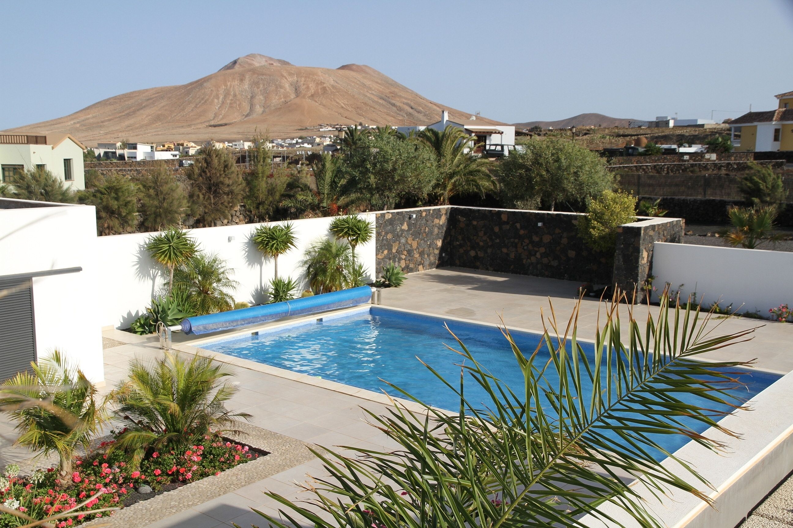 Una piscina con una montaña al fondo, rodeada de follaje y un muro de piedra.
