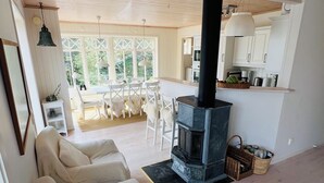 Ein gemütliches Wohnzimmer mit Kamin, ein Essbereich mit weißen Stühlen und eine Küche mit weißen Schränken.