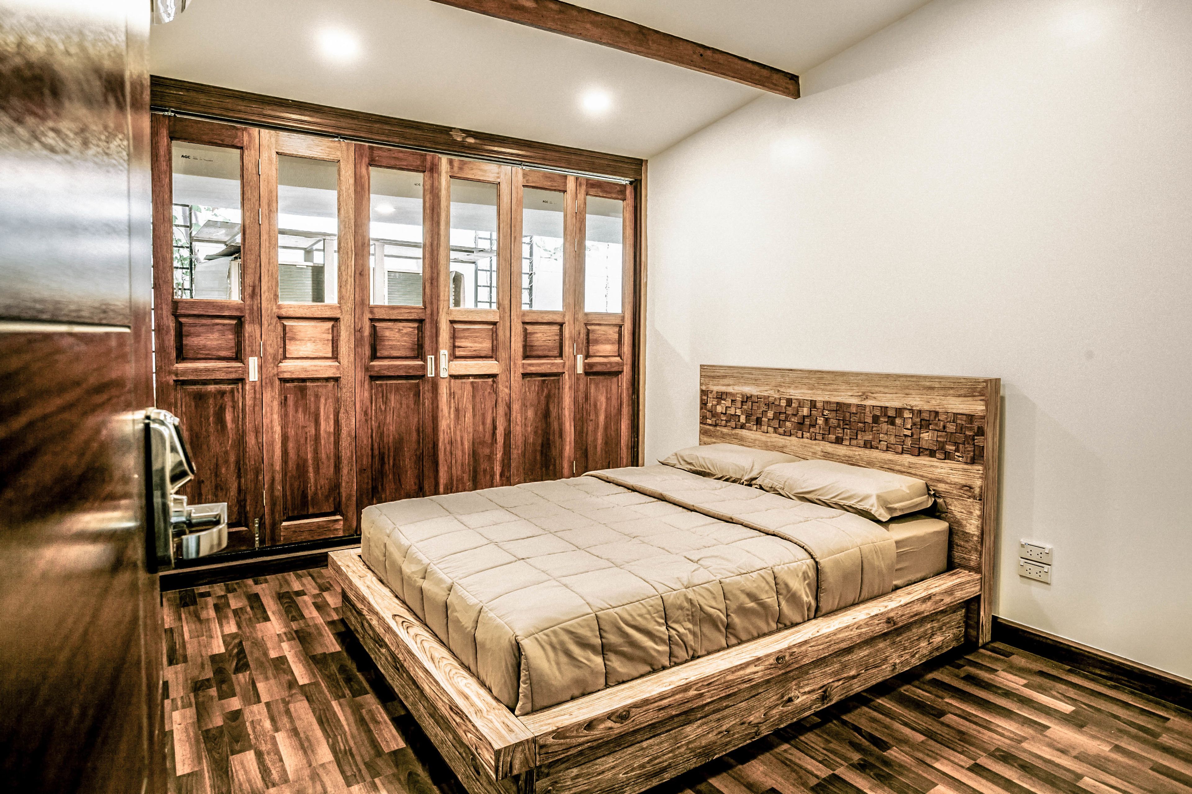 Une chambre à coucher avec un lit en bois, une grande armoire aux portes miroir et un parquet à motifs en chevrons.