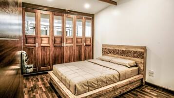 Une chambre à coucher avec un lit en bois, une grande armoire aux portes miroir et un parquet à motifs en chevrons.