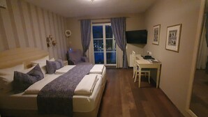A hotel room with two beds, a desk, a chair, a TV, and a window with curtains. - Suite - Hotel Leeberghof (Tegernsee)