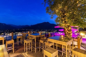 An outdoor seating area with wicker furniture and a view of a cityscape and mountains at dusk. - Double room - Hotel Leeberghof (Tegernsee)