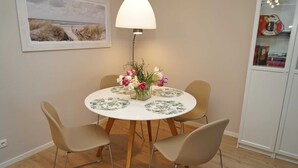 Een eetruimte met een ronde tafel, vier stoelen, een bloemenvaas, een lamp en een boekenkast.
