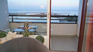 Een balkon met uitzicht op zee en een pier. Er staat een tafel met stoelen en een bloempot.