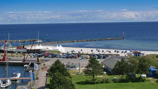 Een kustjachthaven met boten aanmeren, een zandstrand en een helderblauwe lucht.