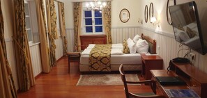 A hotel room with a bed, bedside table, chair, television, and a window with curtains.