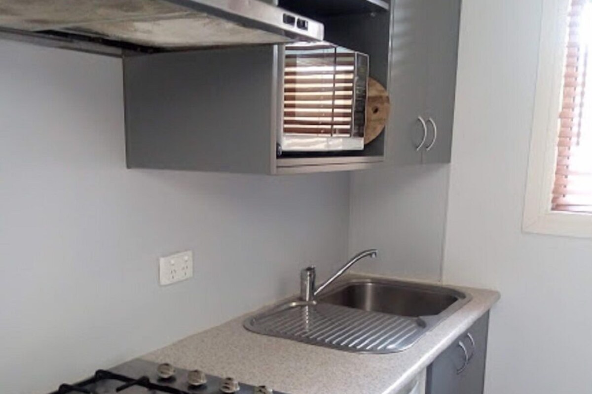 A compact kitchen with a gas stove, a sink, and grey cabinets.