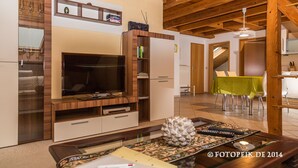 Un salon avec un téléviseur, un meuble de rangement en bois et un coin repas avec une table verte.