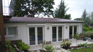 Un bâtiment d’un seul étage, doté d’un toit en tuiles, de grandes portes-fenêtres coulissantes et d’un petit jardin agrémenté de pas japonais et de plantes.