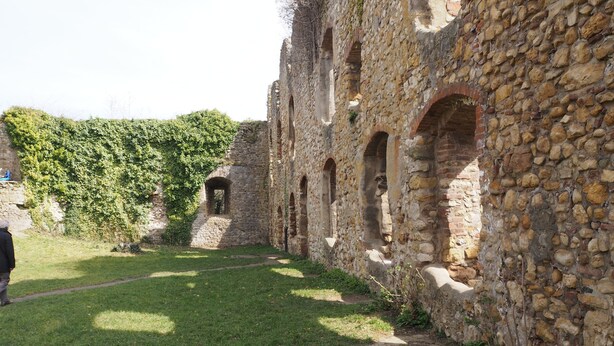Un ancien bâtiment en pierre, doté d’arcades et d’une cour verdoyante.