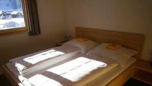 A bed with white linens, a wooden headboard, and a nightstand with a lamp.