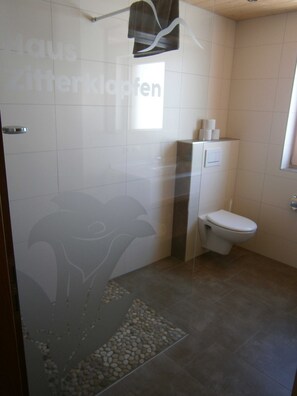 Ein Badezimmer mit Dusche, Toilette und einer Wandverkleidung.