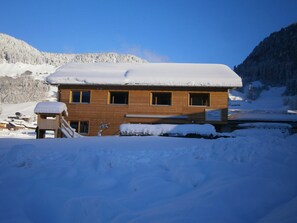 Ein Holzbau mit verschneitem Dach, umgeben von verschneiter Landschaft und Bergen.