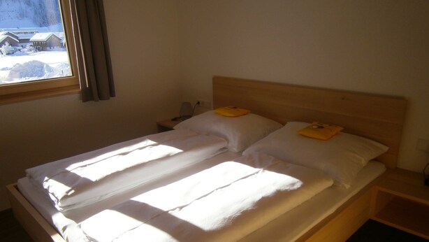 Un lit avec du linge de lit blanc, une tête de lit en bois et une table de chevet avec une lampe.